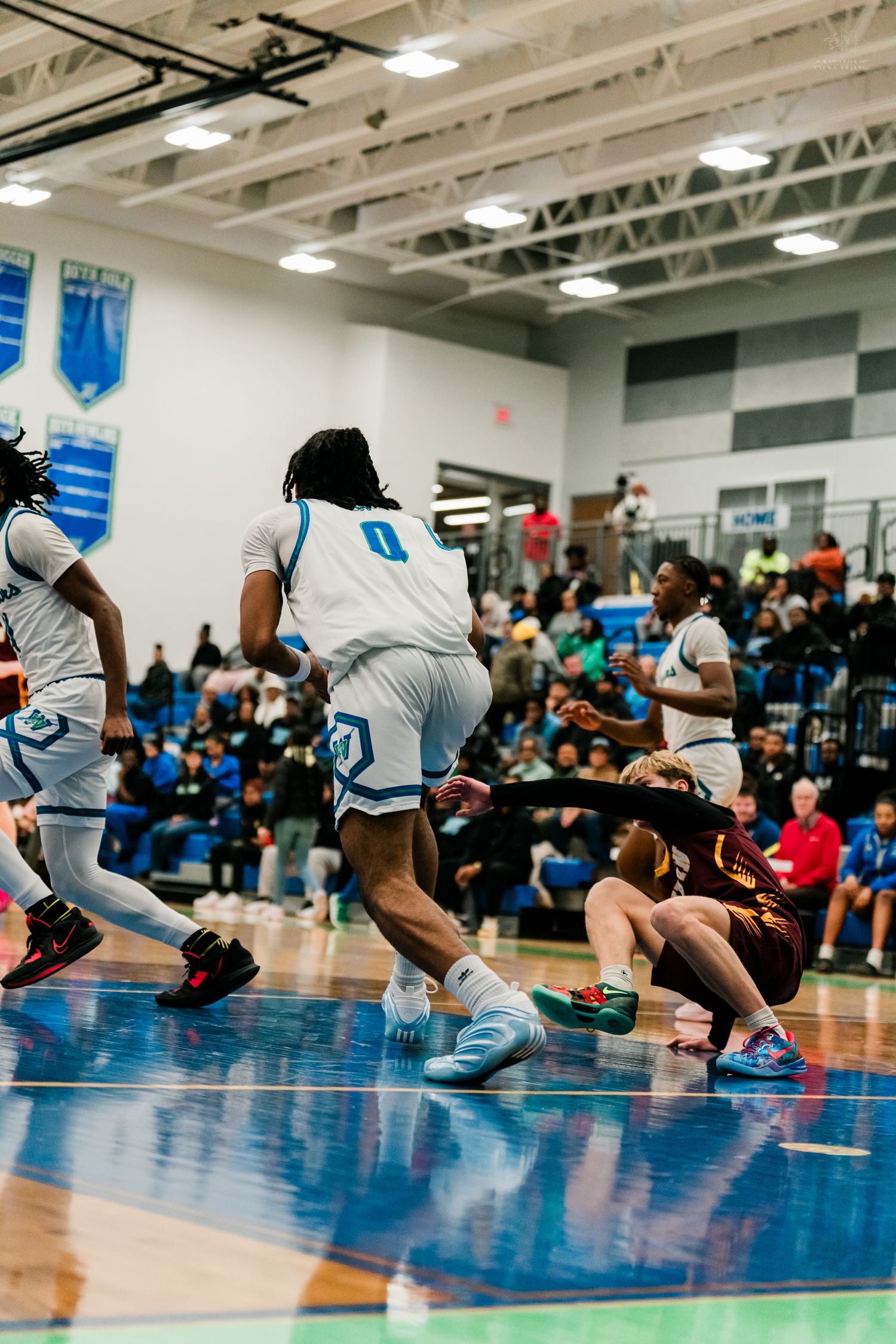Number 0 home team player drives past fallen Turpin opponent during intense high school basketball game with full crowd.