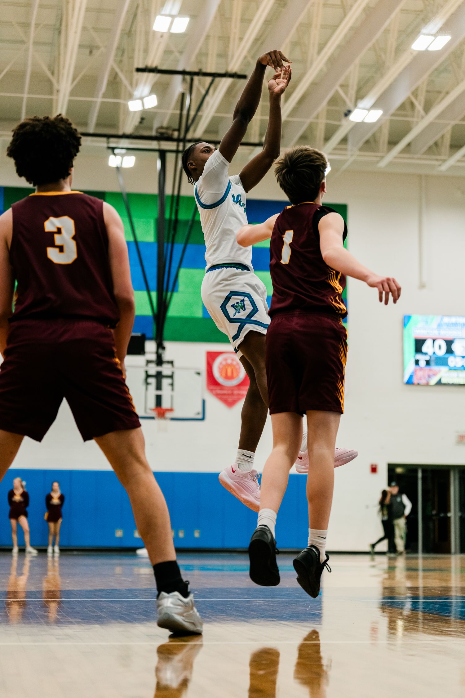 Warriors player in white leaps for a layup over a maroon-uniformed defender during a high school game.