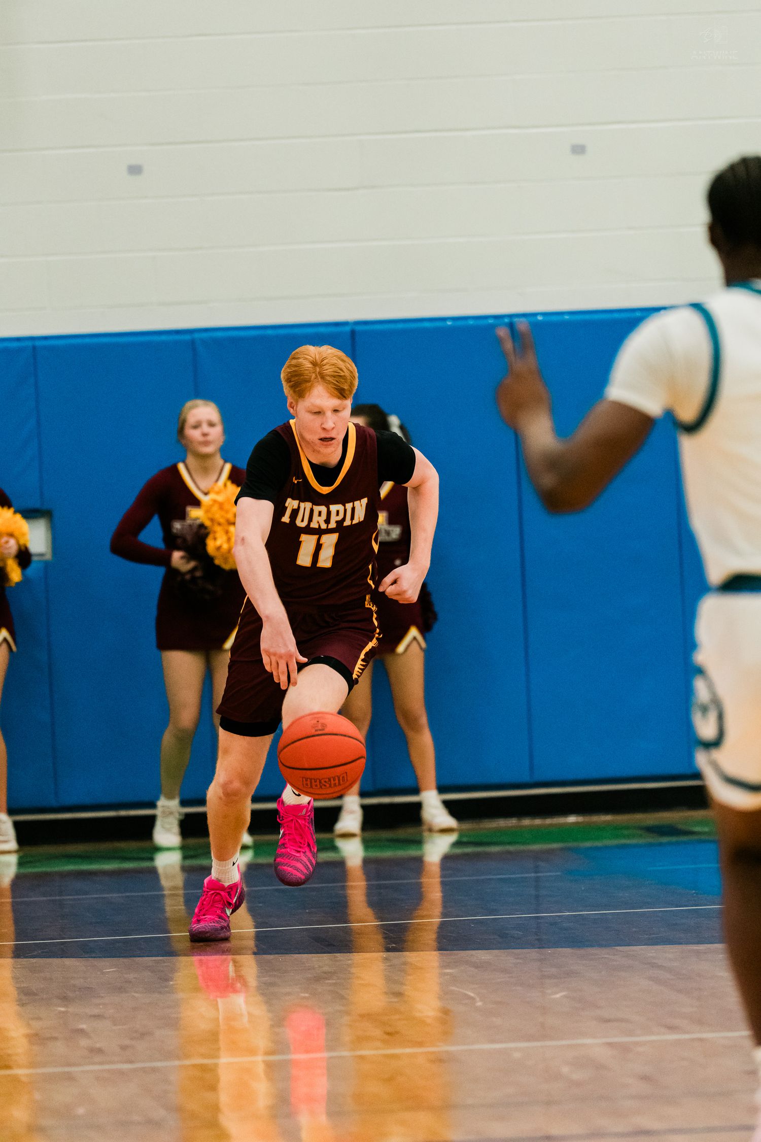 Turpin High School player number 11 dribbles the basketball while being guarded during an indoor basketball game.