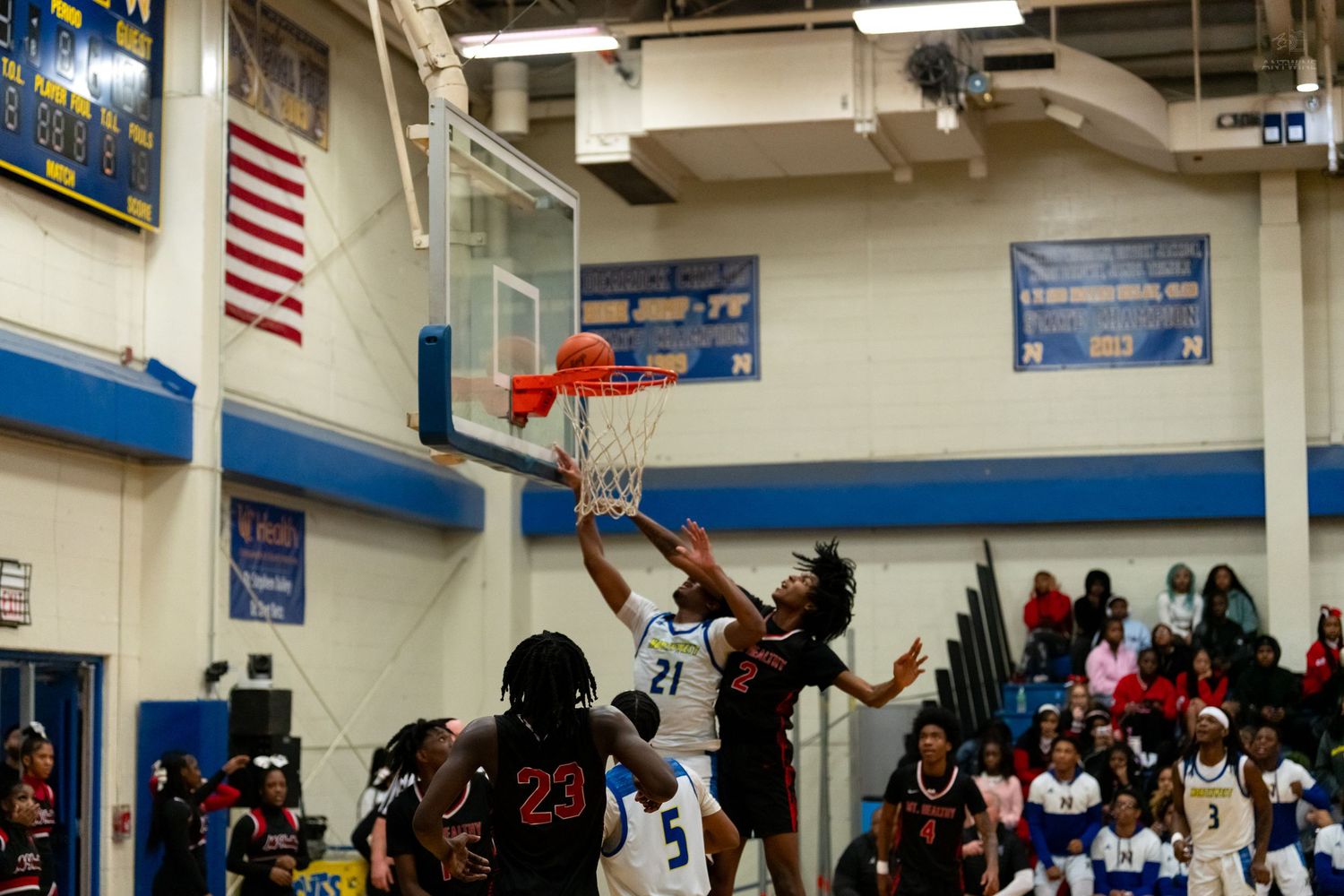A basketball player dunks during an intense high school game while opponents attempt to block the shot.