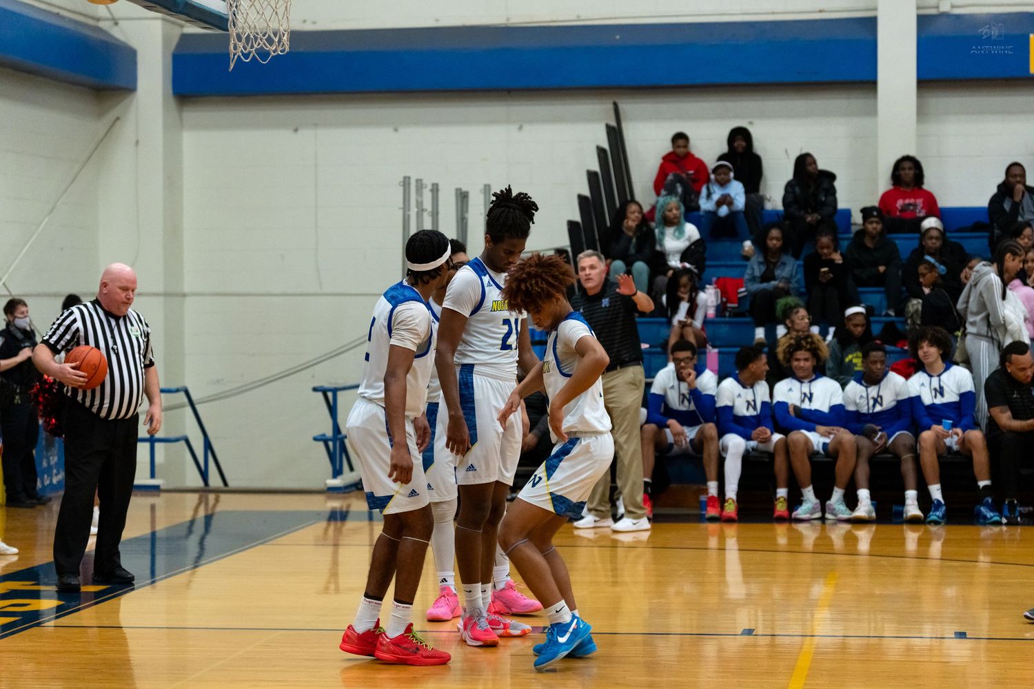 Three high school basketball players in white uniforms huddle together during an indoor basketball game.