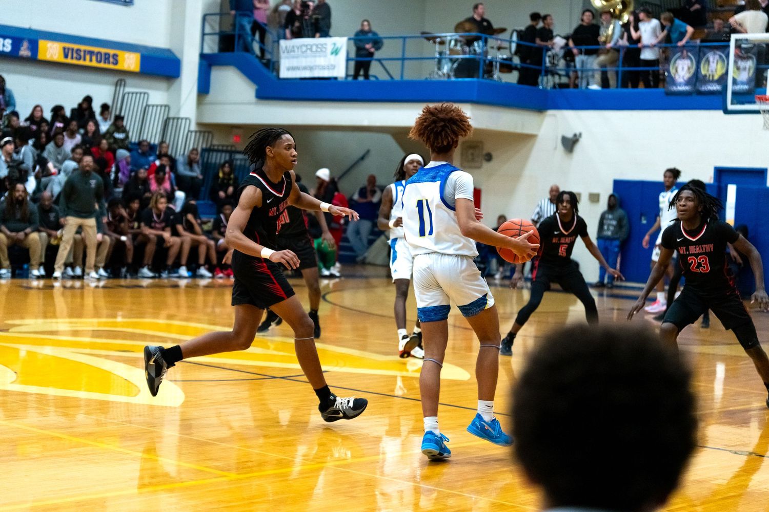 Player in blue number 11 jersey drives past defenders during a competitive high school basketball game.