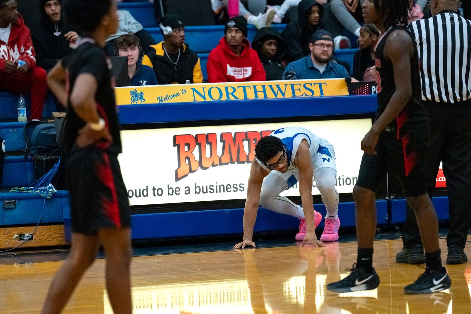 Northwest High School basketball player crouches on the court during a game with opponents nearby.