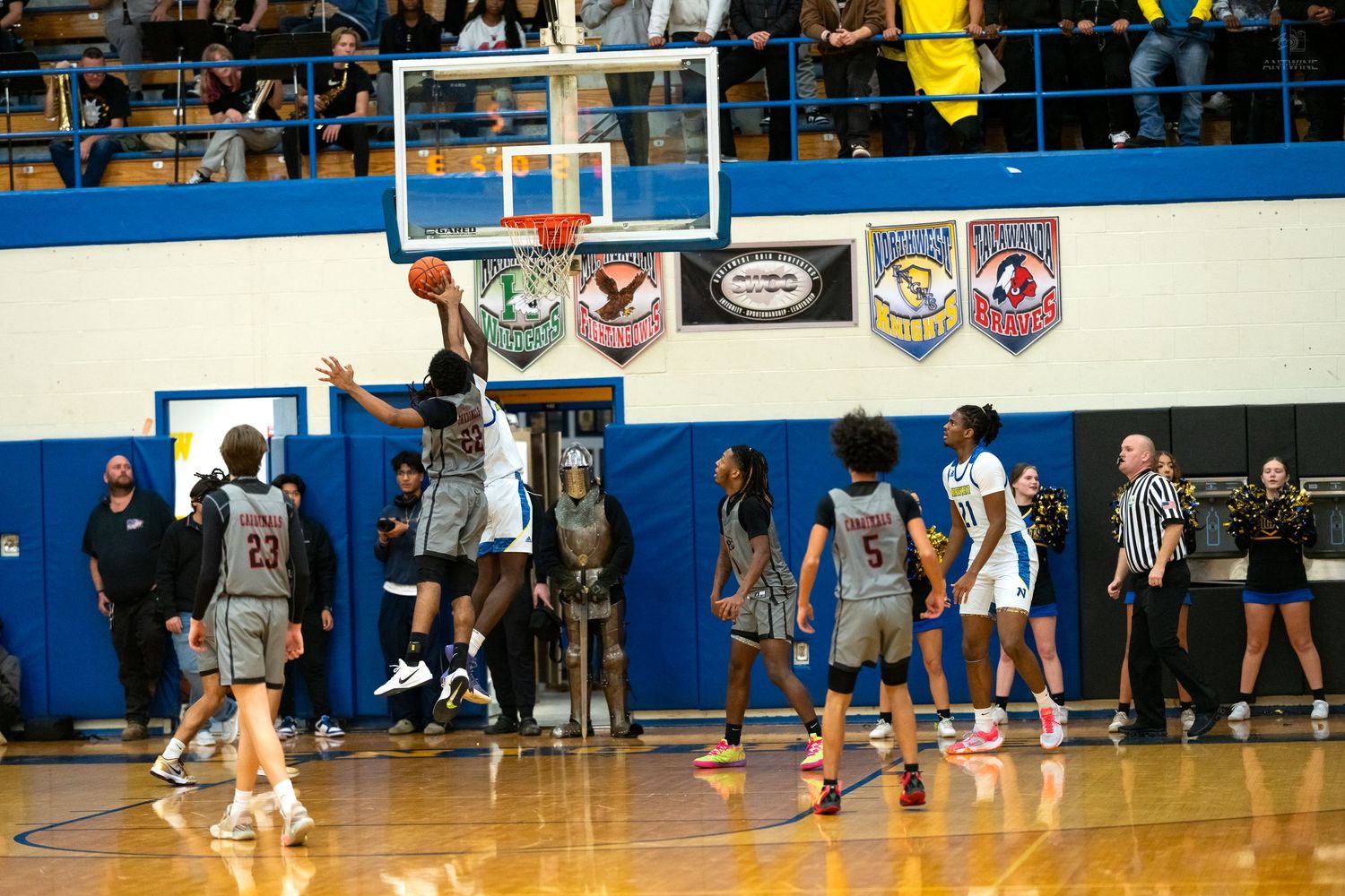 Basketball player attempts a shot near the hoop during a competitive high school gymnasium game with spectators watching.