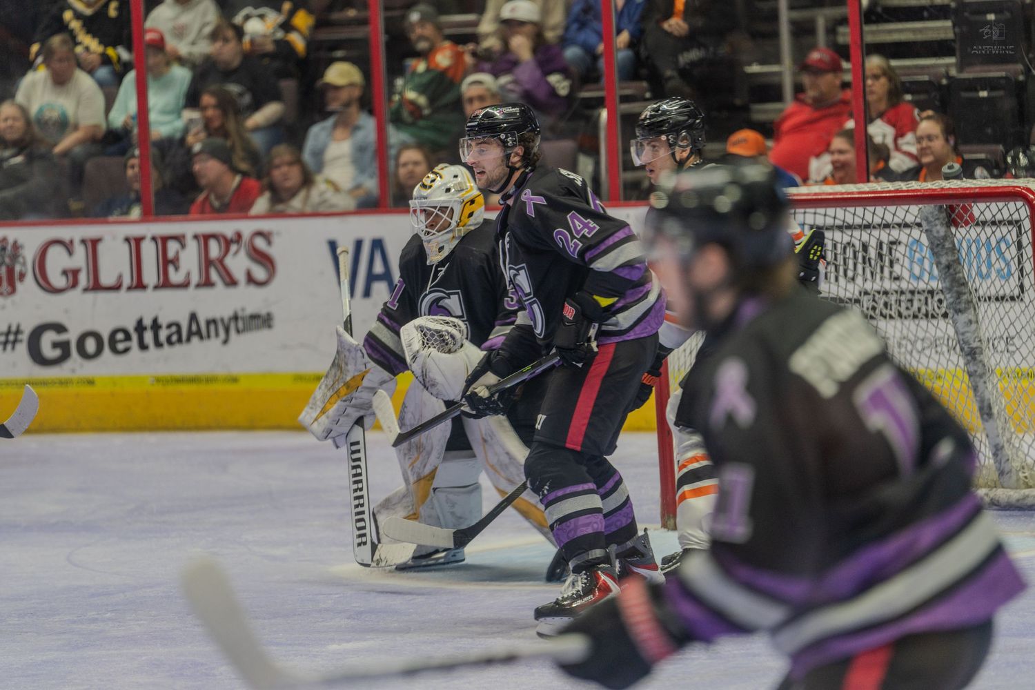 A hockey player in purple positions in front of the goal as the goalie prepares to defend.