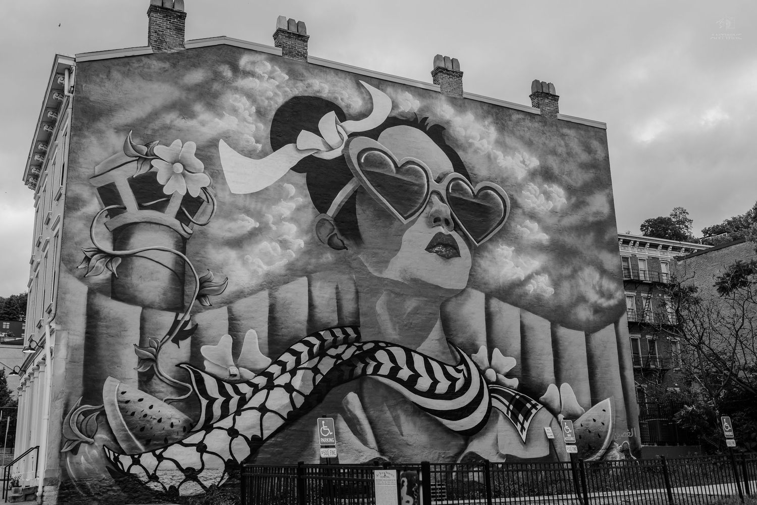 Large colorful street art mural of a woman with heart-shaped sunglasses on a city building exterior.