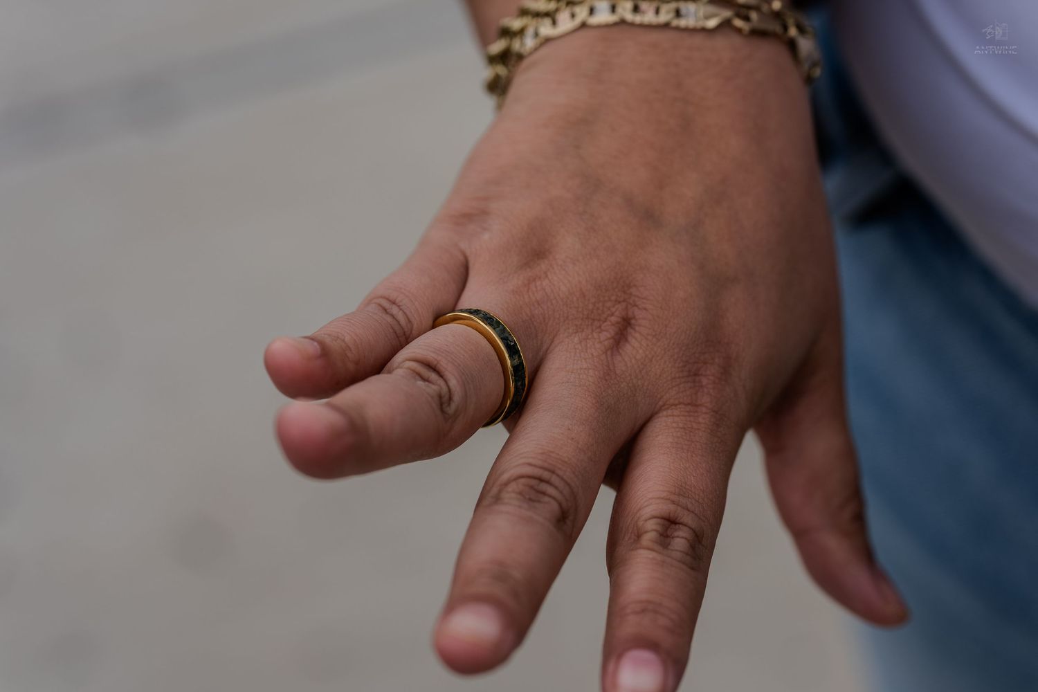 Close-up of a hand wearing a gold and black band ring with a gold chain bracelet.
