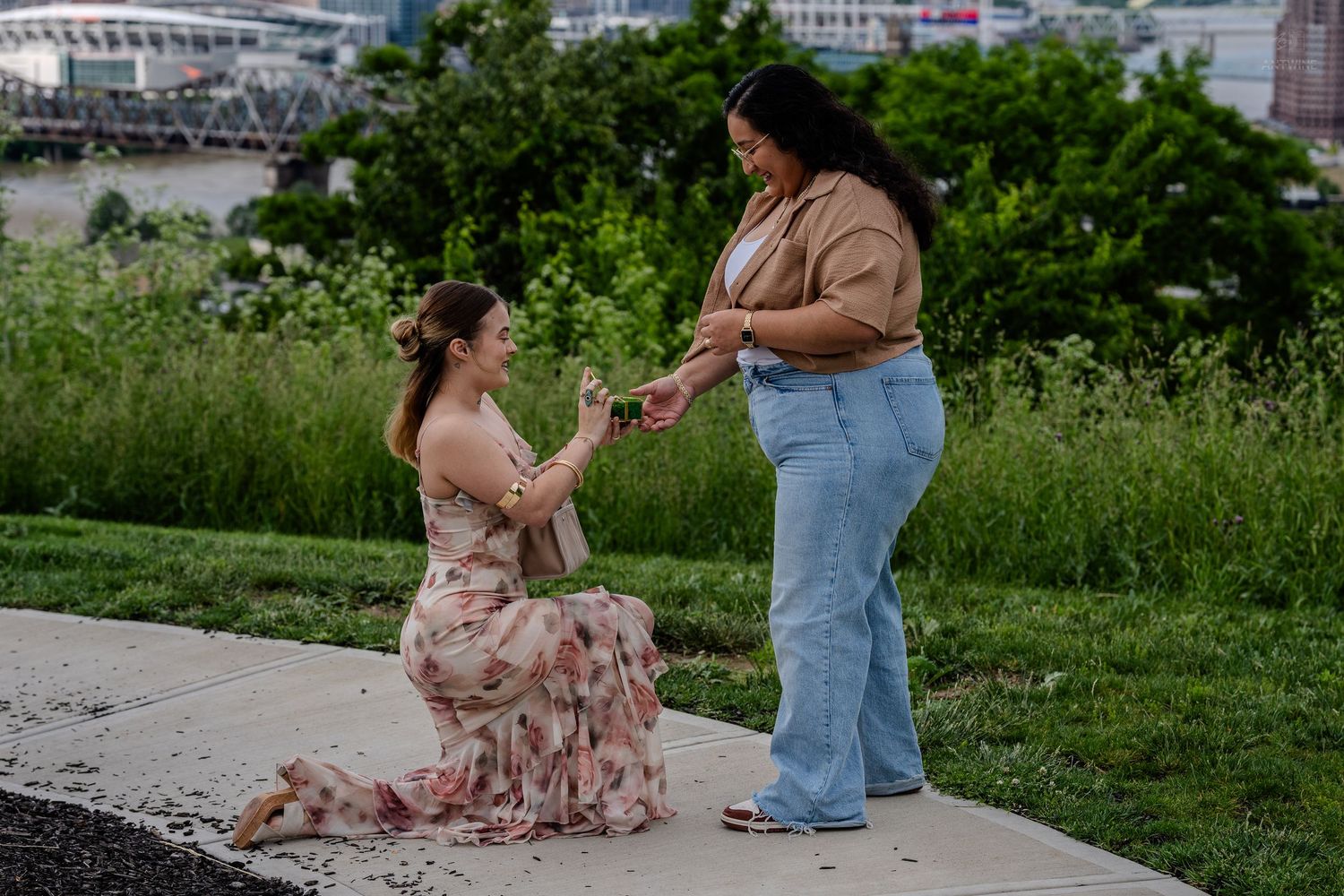 Color photo of woman in floral dress proposing to partner on sidewalk.