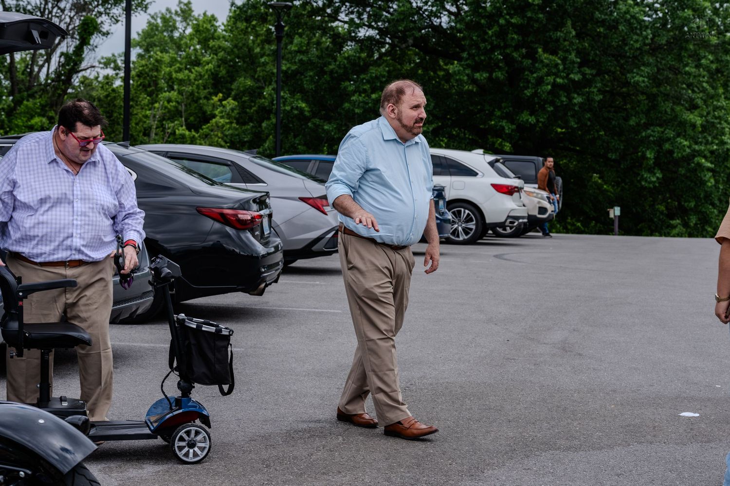 Two men in a parking lot near a mobility scooter on a cloudy day.