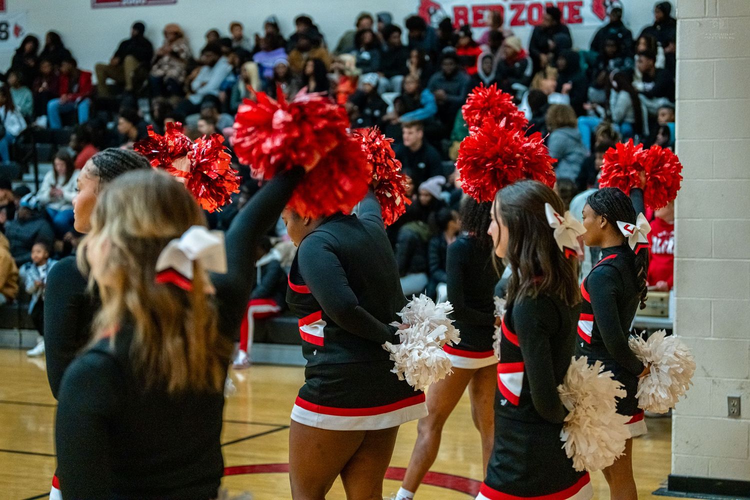 Cheerleaders in black and red uniforms wave red and white pom-poms during a high school basketball game.