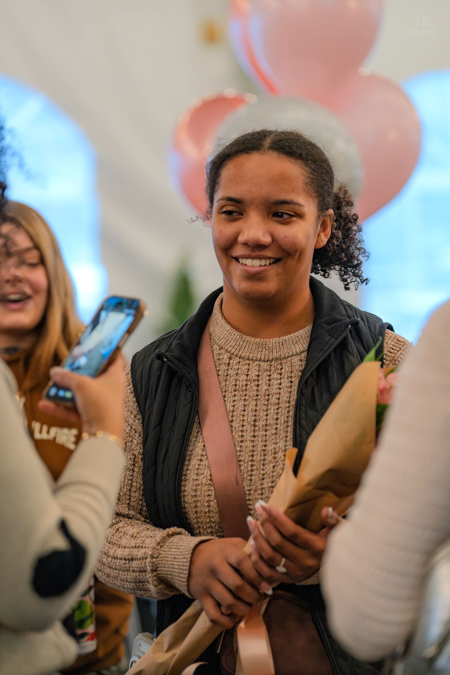 A happy young woman holds a bouquet of flowers while smiling among friends at a festive celebration.