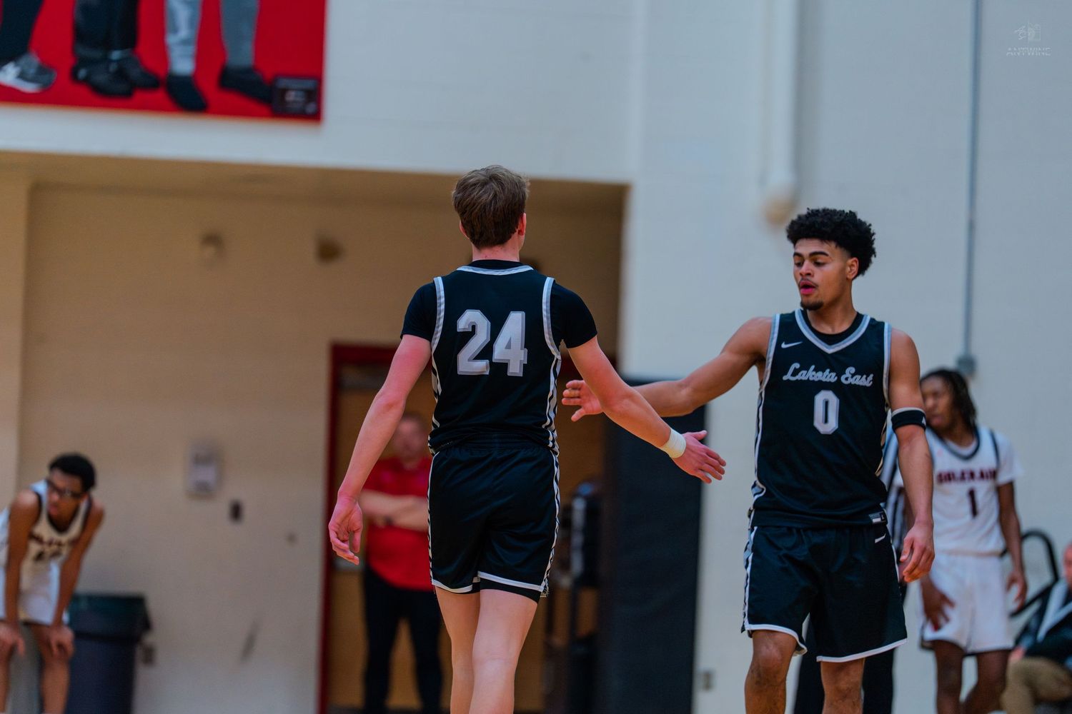 Two Lakers basketball players #24 and #0 exchange high five during high school game.