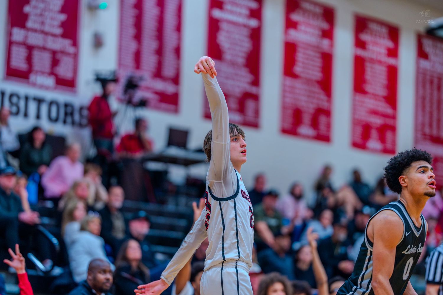 High school basketball player shoots a free throw with follow-through form in a packed gymnasium.