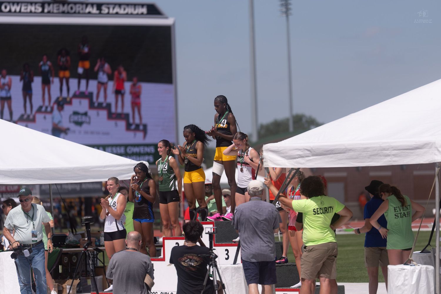 Female track athletes pose on the awards podium at Owens Memorial Stadium during a championship meet.