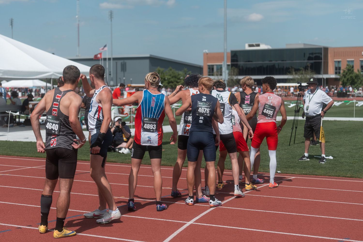 High school track athletes in various uniforms gather together on red track after relay race competition.