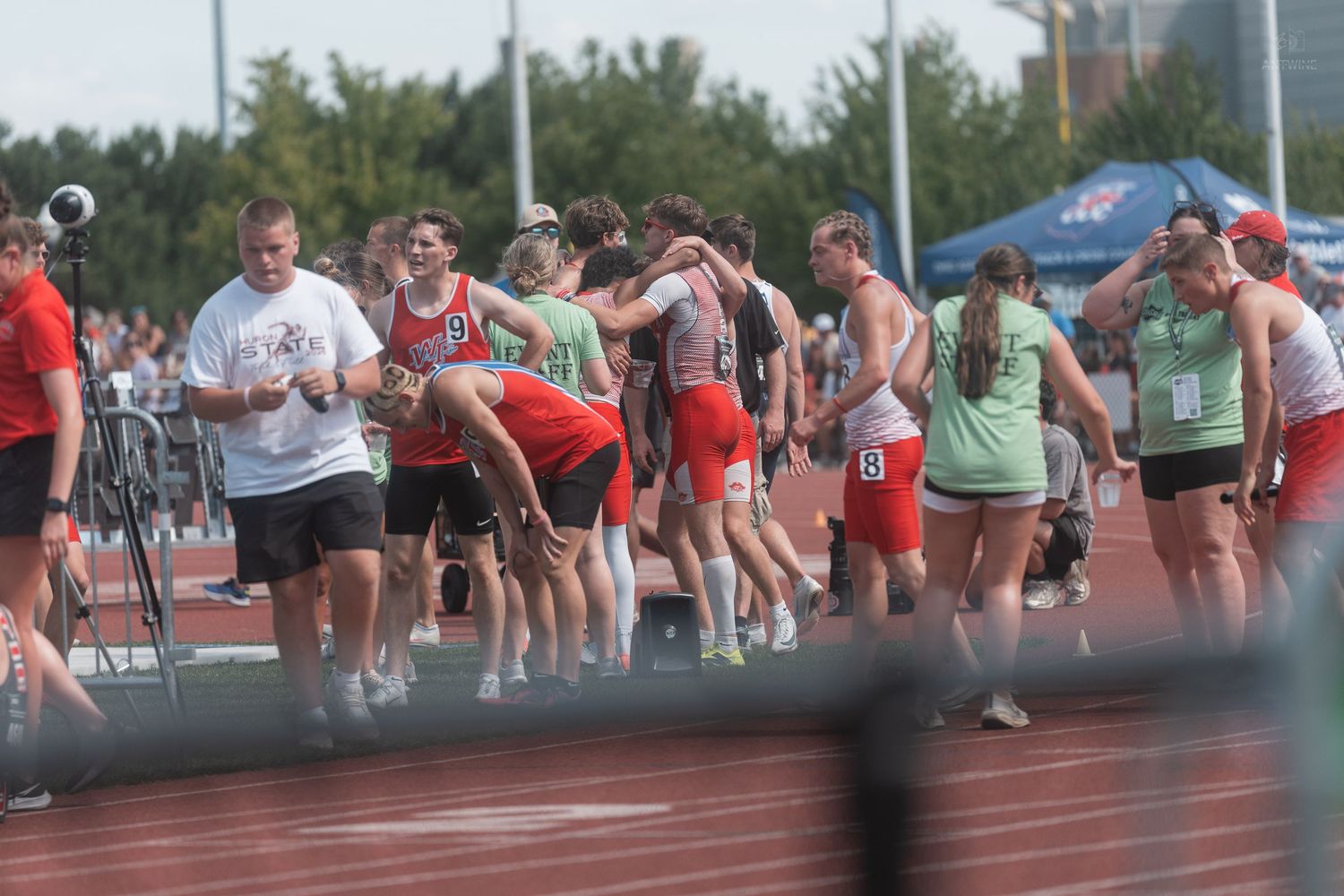 Track and field athletes and coaches gather on the track after a competitive relay race event.