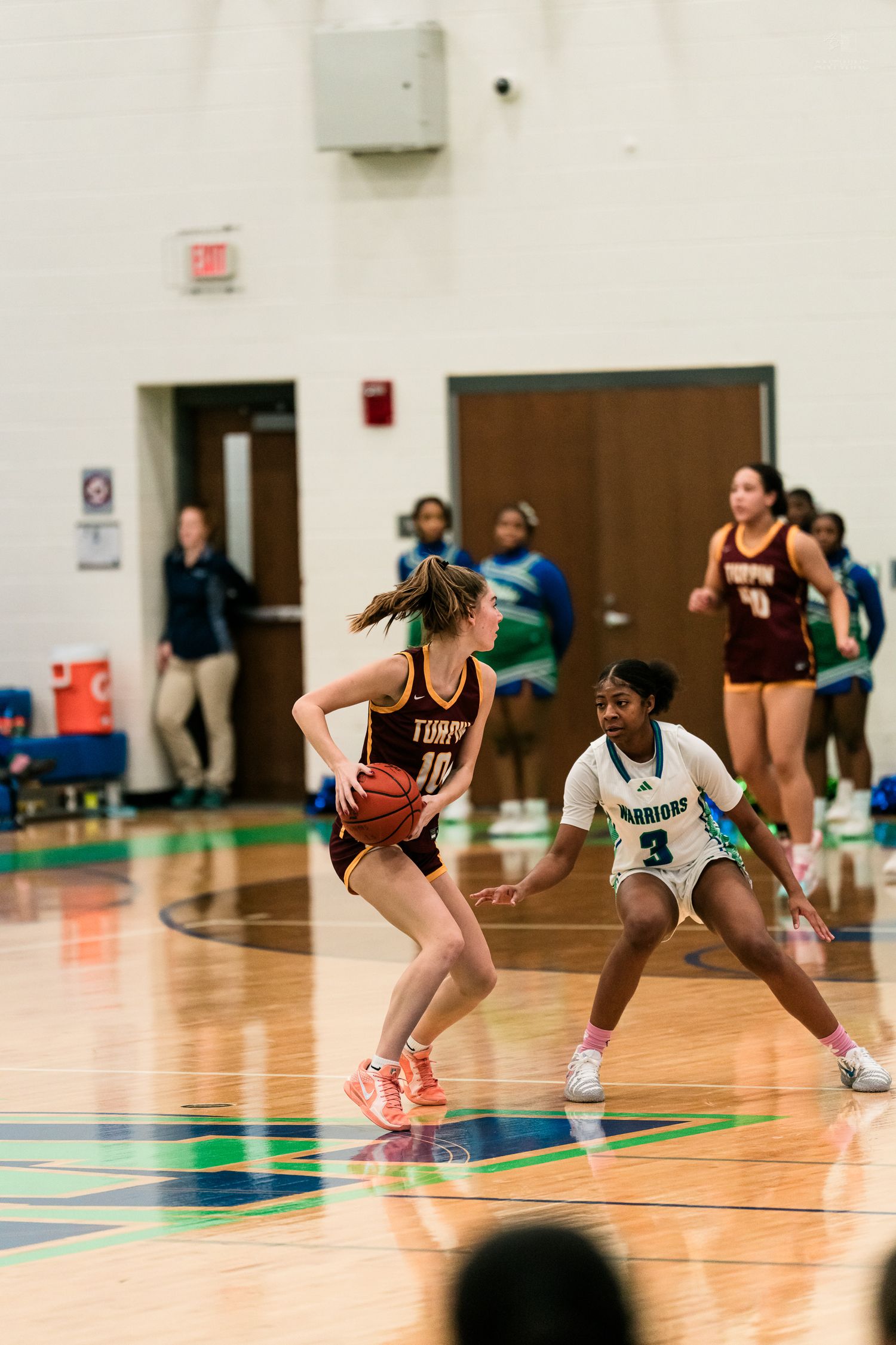 A girls high school basketball player in maroon number 10 handles the ball while a Warriors defender guards her.