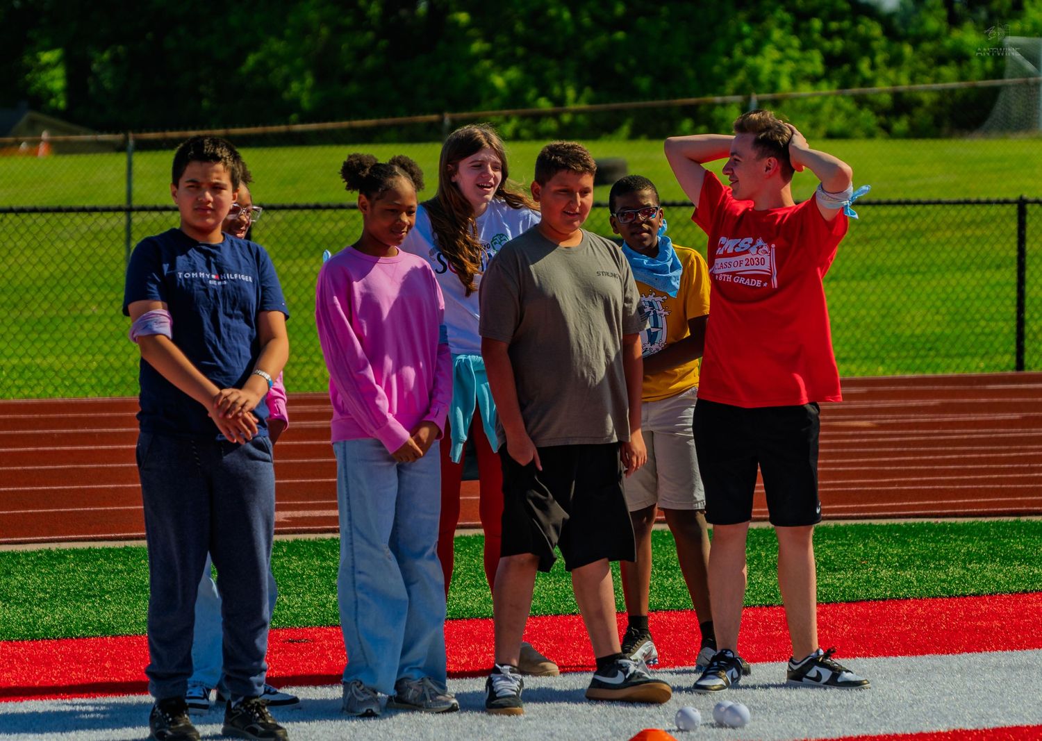 Group of middle school students standing on a red track during an outdoor field day activity on a sunny day.