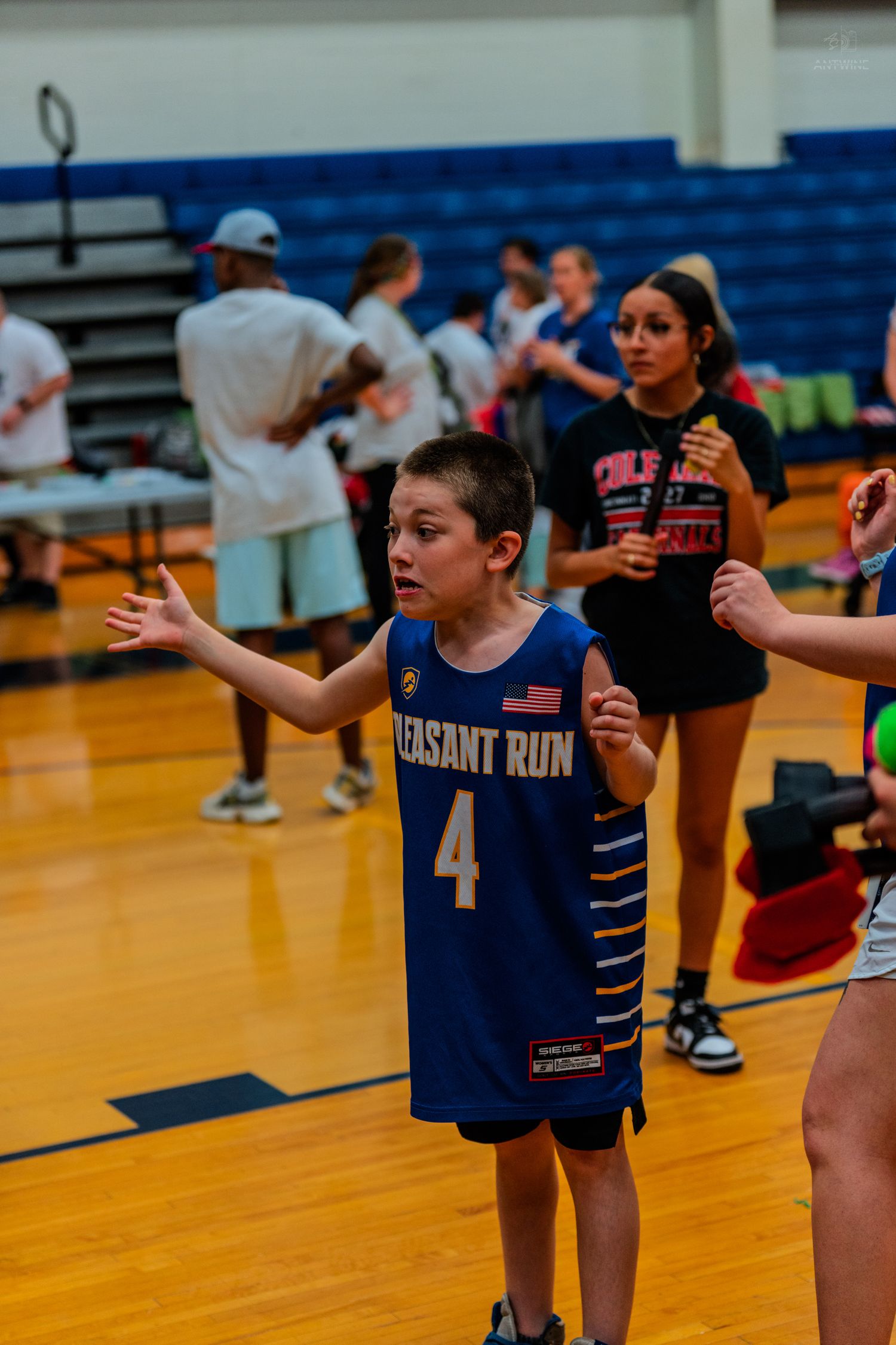 Young boy in Pleasant Run #4 basketball jersey stands with arms outstretched on indoor court during youth game.