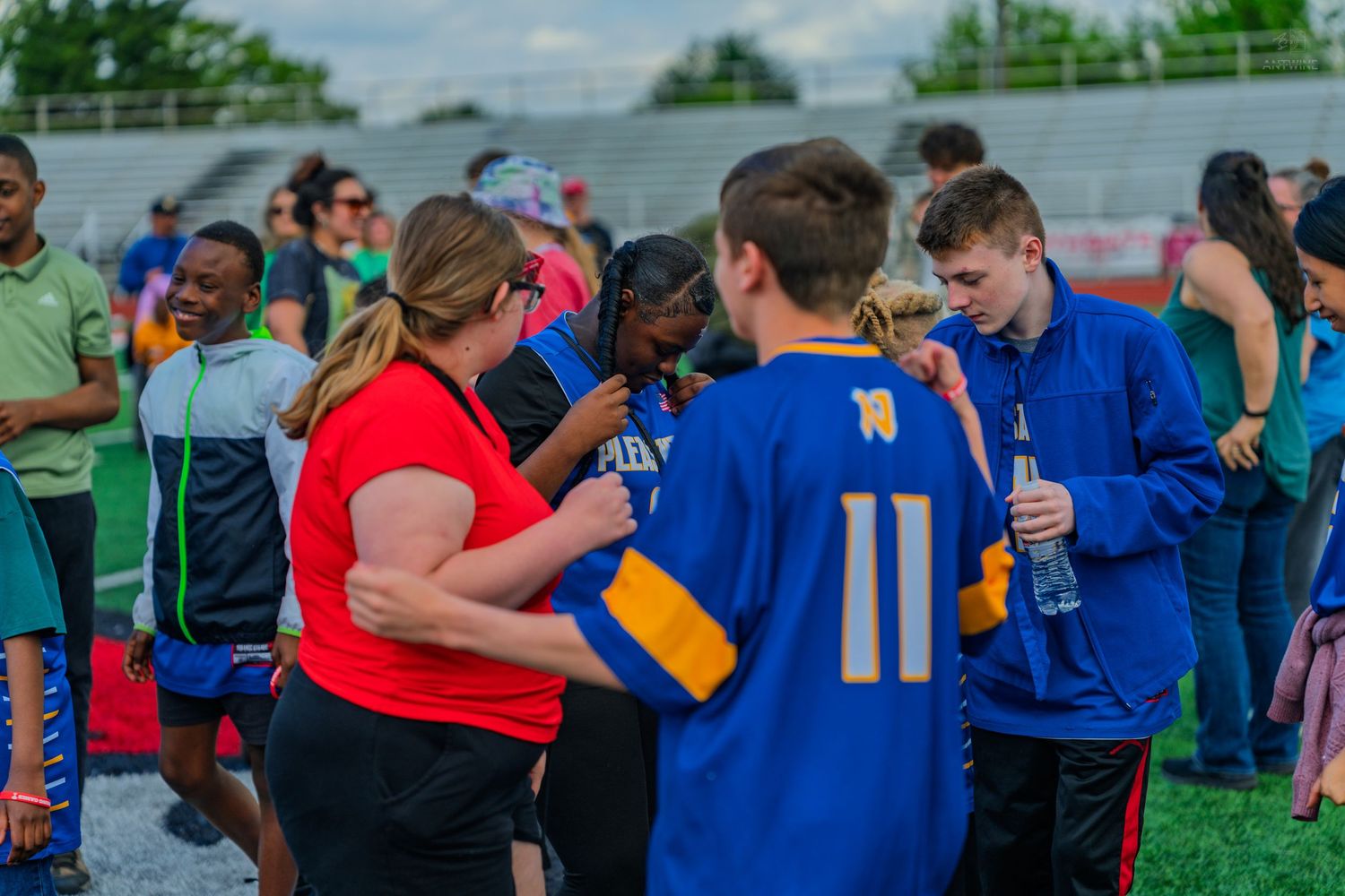 Group of teens and adults gathered on a sports field during an outdoor event, wearing colorful jerseys and casual attire.