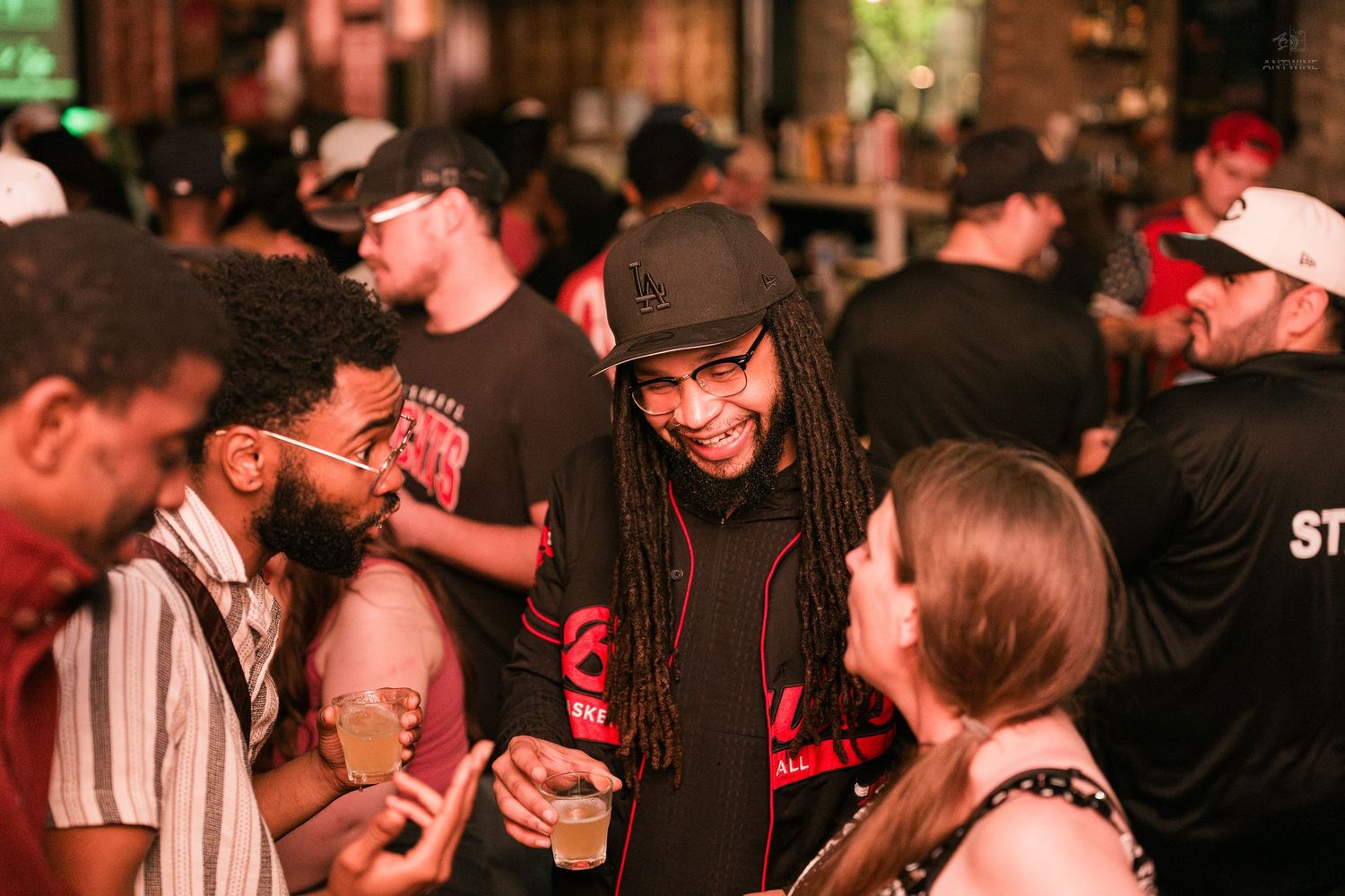 Man with dreadlocks laughing and socializing with guests at a nightclub party.