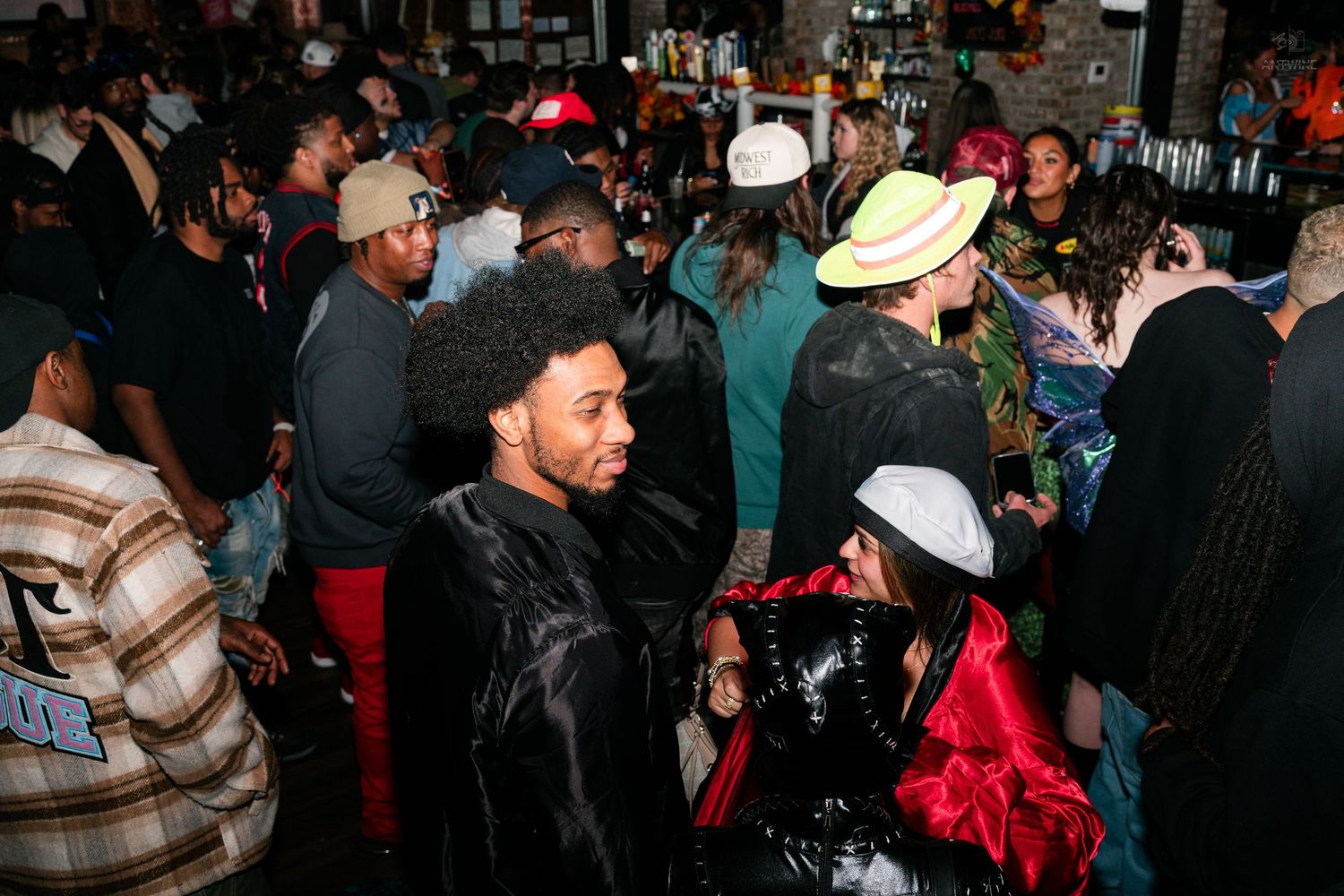 Diverse crowd of partygoers in Halloween costumes at a busy bar event.