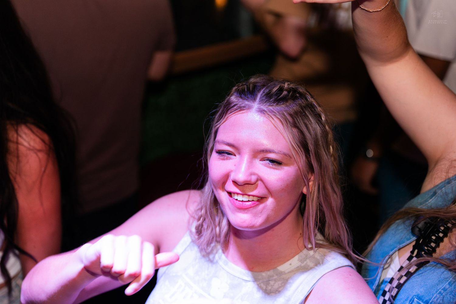 Smiling blonde woman giving thumbs up at a fun nightclub party.