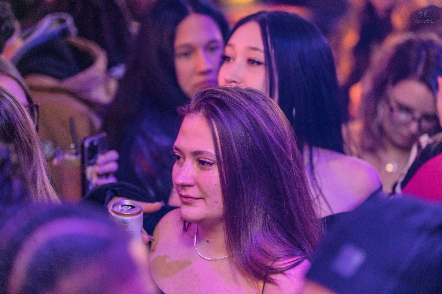 A woman with long dark hair stands in a crowded venue under purple ambient lighting.