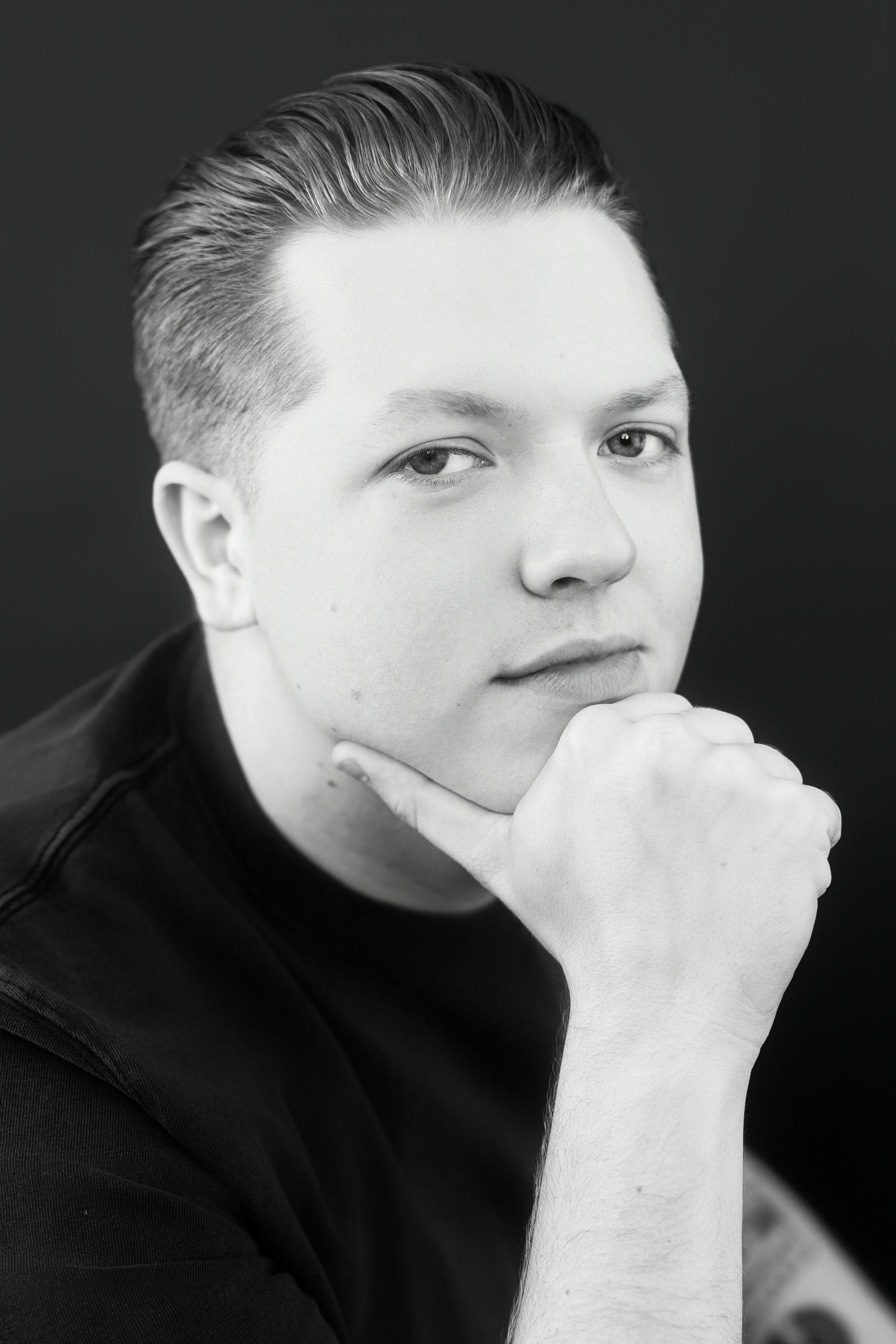 Black and white portrait of young man resting chin on fist, contemplative expression.
