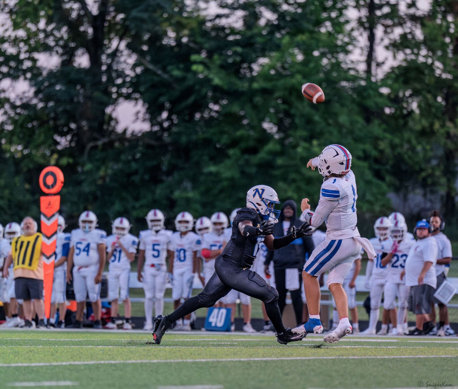 Defensive player pressures quarterback during evening high school football game.