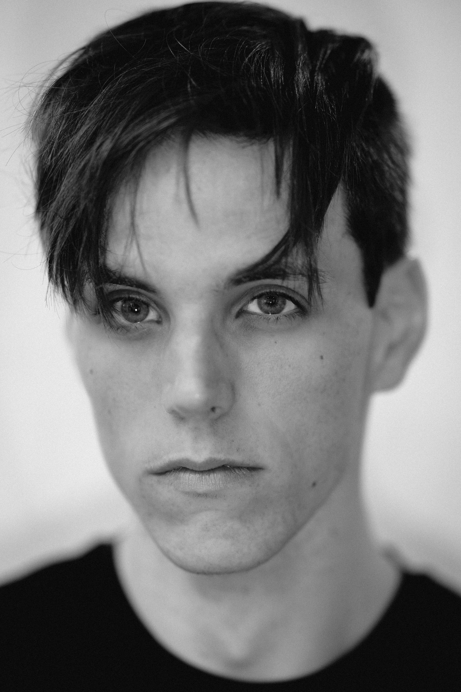 Dramatic black and white close-up portrait of a young man with dark swept hair and intense gaze.