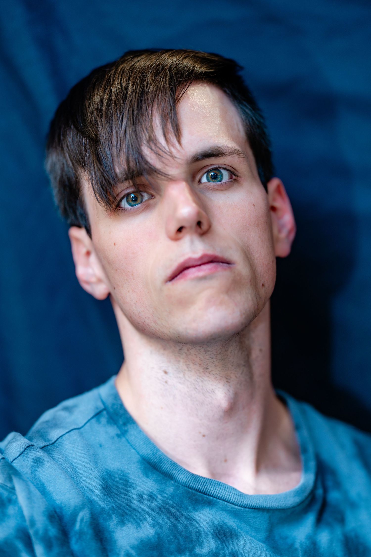 Young man with dark side-swept hair and blue eyes wearing blue tie-dye shirt.