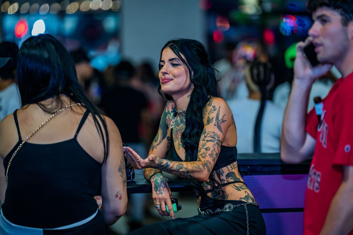 Tattooed woman smiling warmly while socializing at a nightclub.