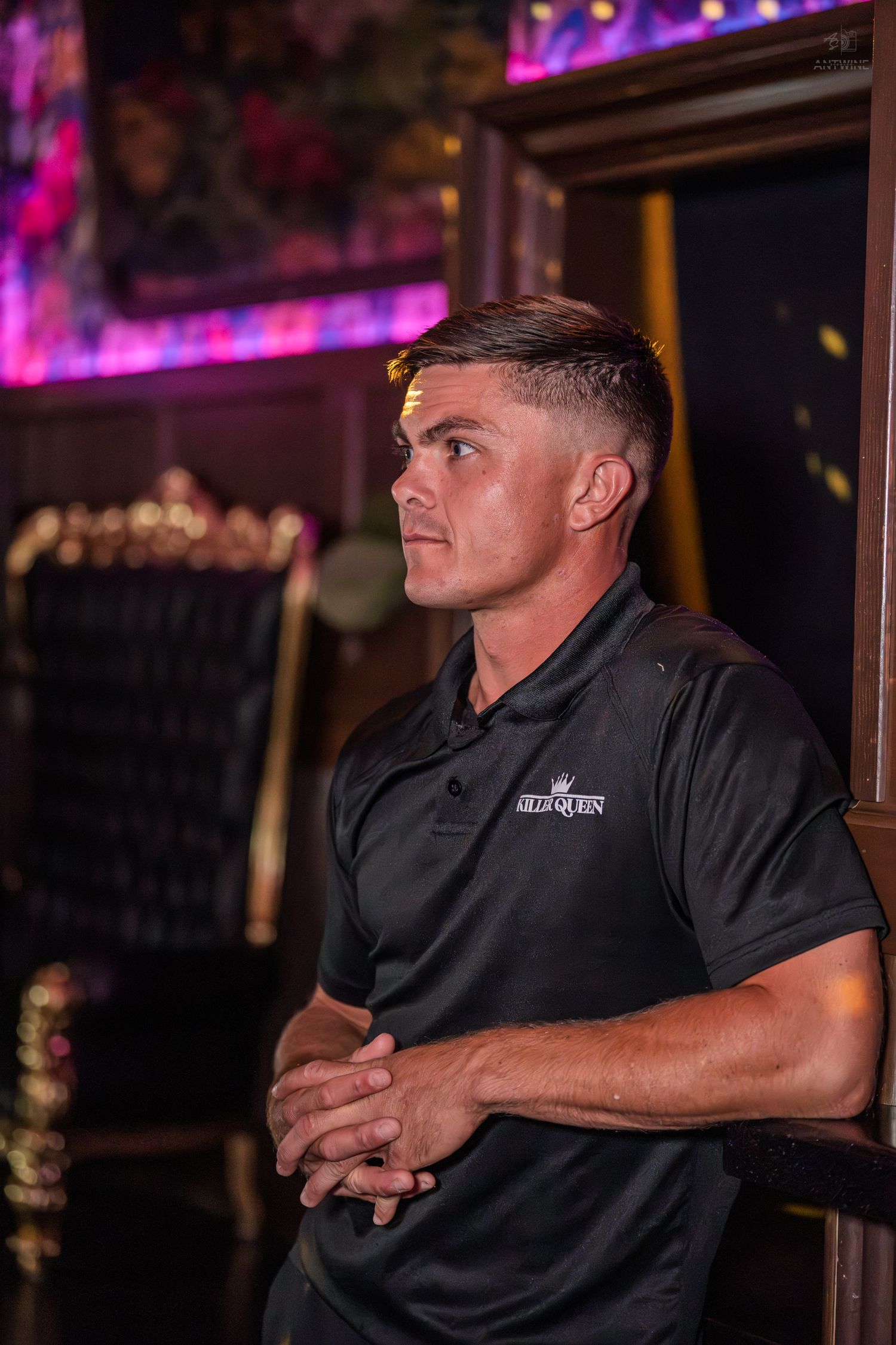 Man in black polo shirt standing attentively inside a dimly lit nightclub.
