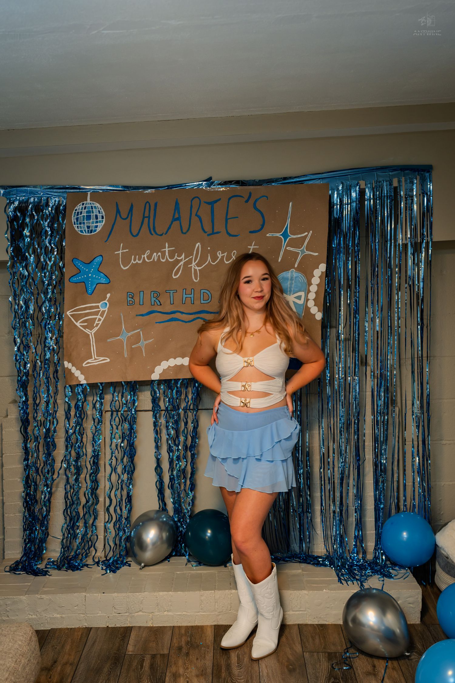 Birthday girl in cream crop top and blue ruffle skirt posing before blue tinsel curtain party backdrop.