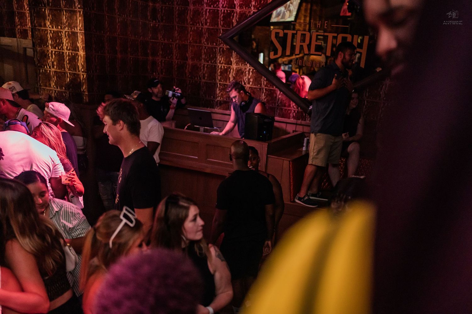 Energetic nightclub crowd surrounds DJ booth at Stretch bar during live music event.