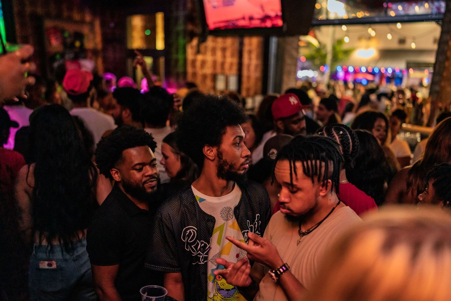 Group of young men socializing at a vibrant nightclub with colorful neon lighting.