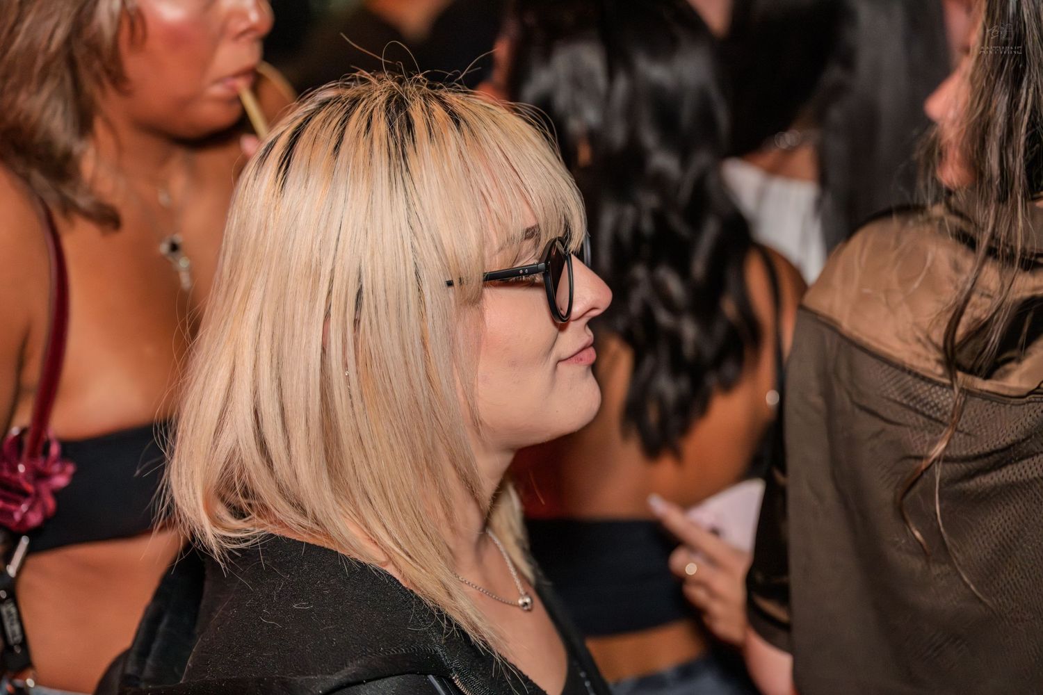 Blonde woman wearing black sunglasses standing in a crowd at an outdoor nighttime event.