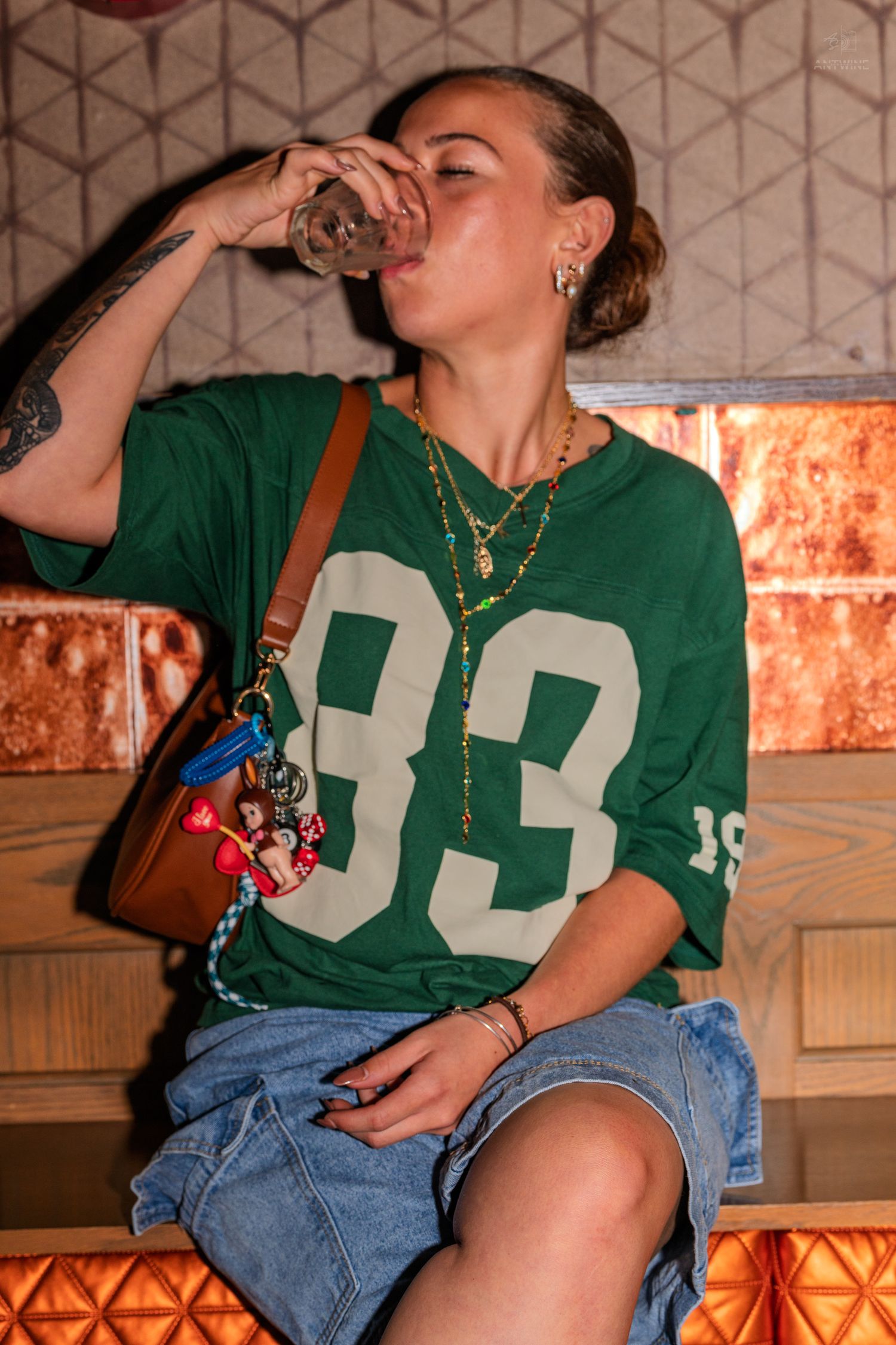 Woman in green jersey number 33 drinking from a glass at a bar.