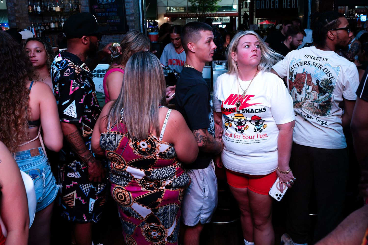 Group of people standing in line outside a bar at night, casual summer attire.