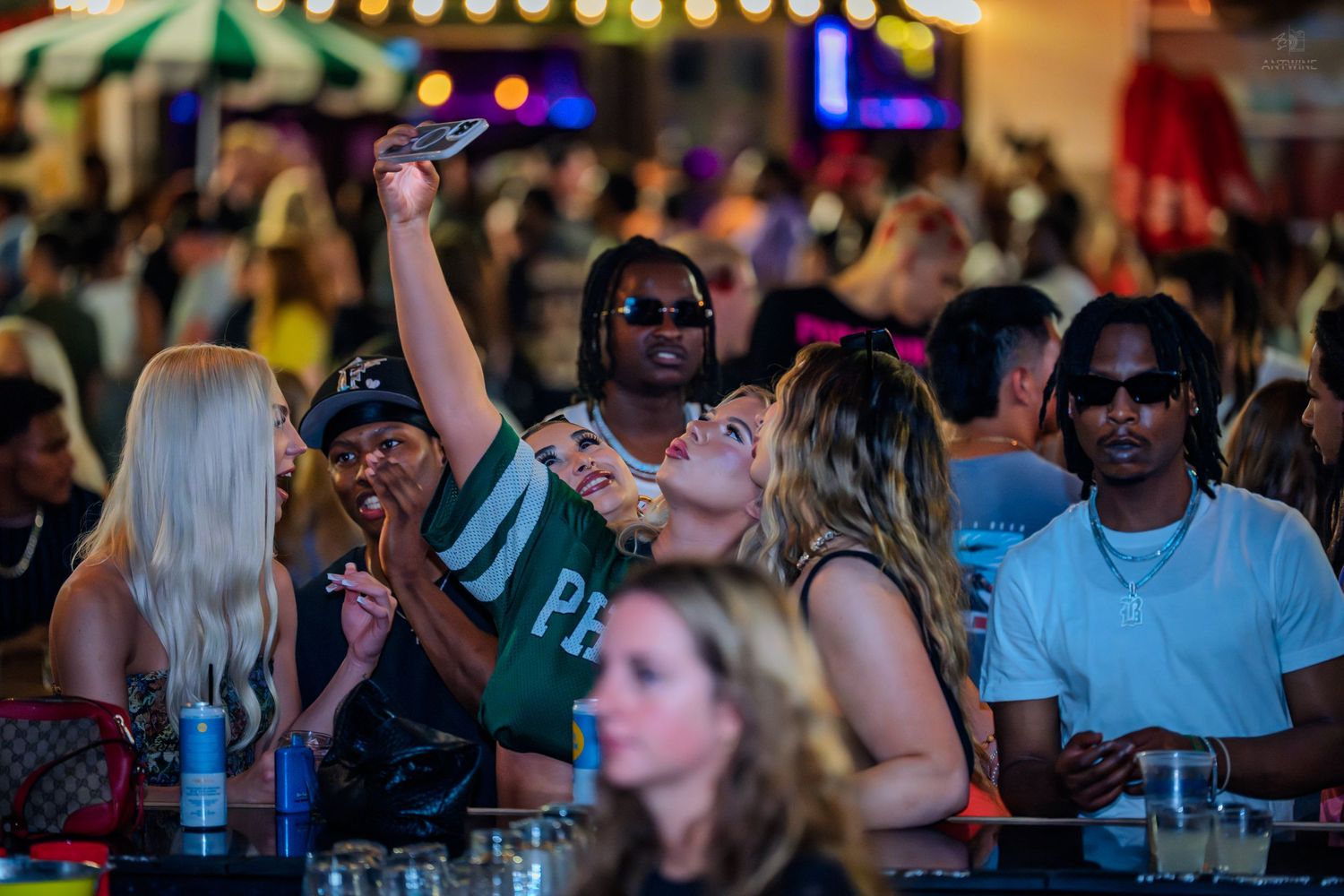 Group of friends taking selfies and socializing at a lively outdoor nightclub event.