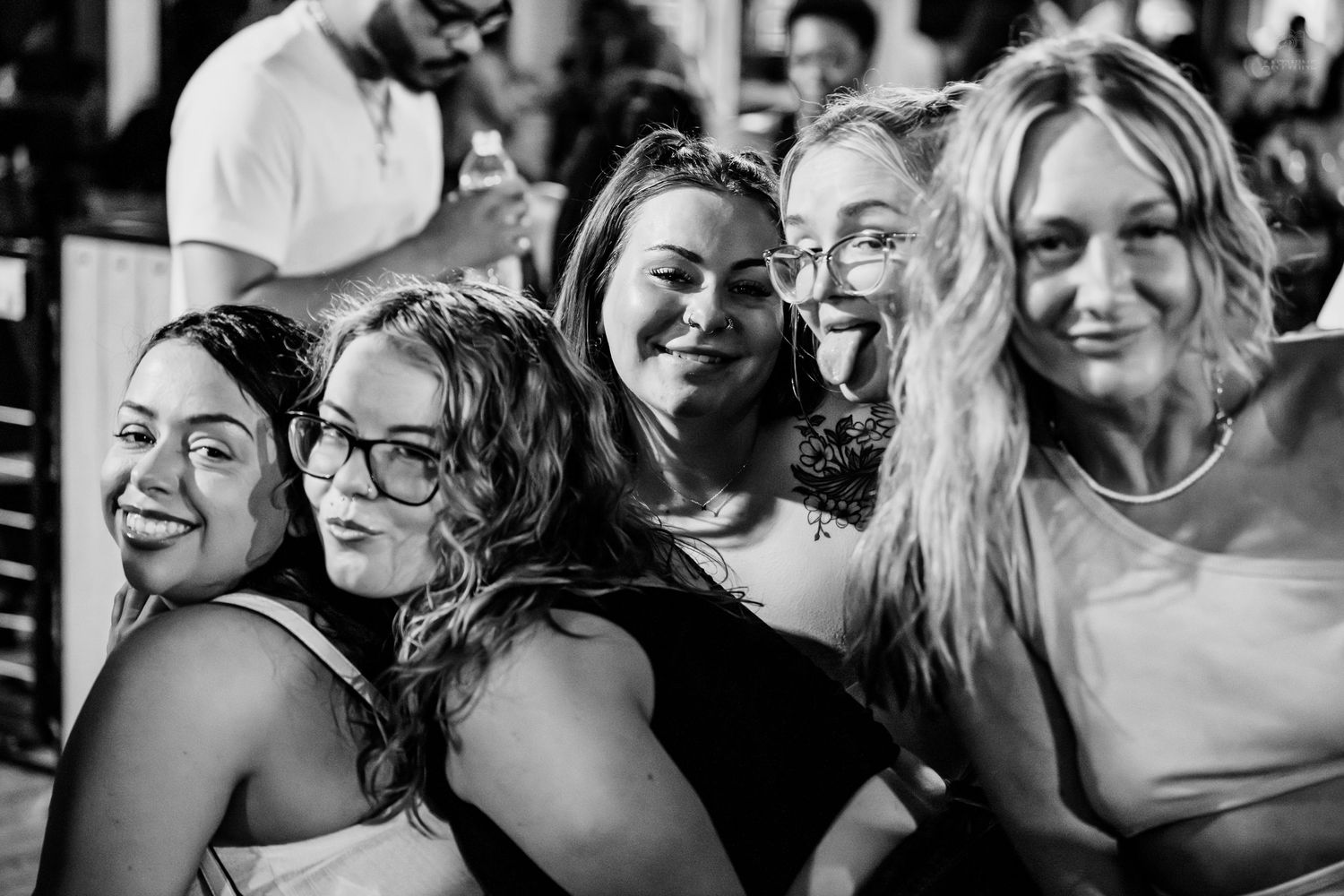 Four women smile together in a black and white photo at a social event.