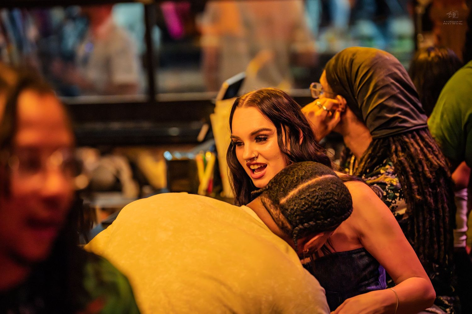 Young woman smiling and hugging someone at a colorful crowded nightlife bar event.