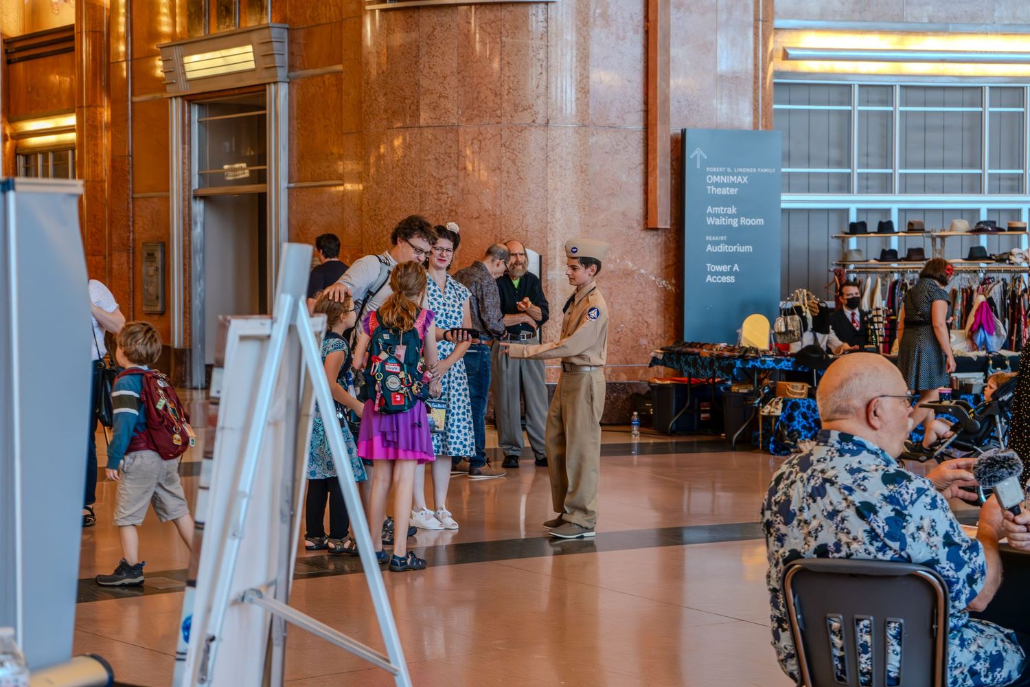 Visitors interact with a uniformed guide in a grand marble lobby during a museum or historic building tour.