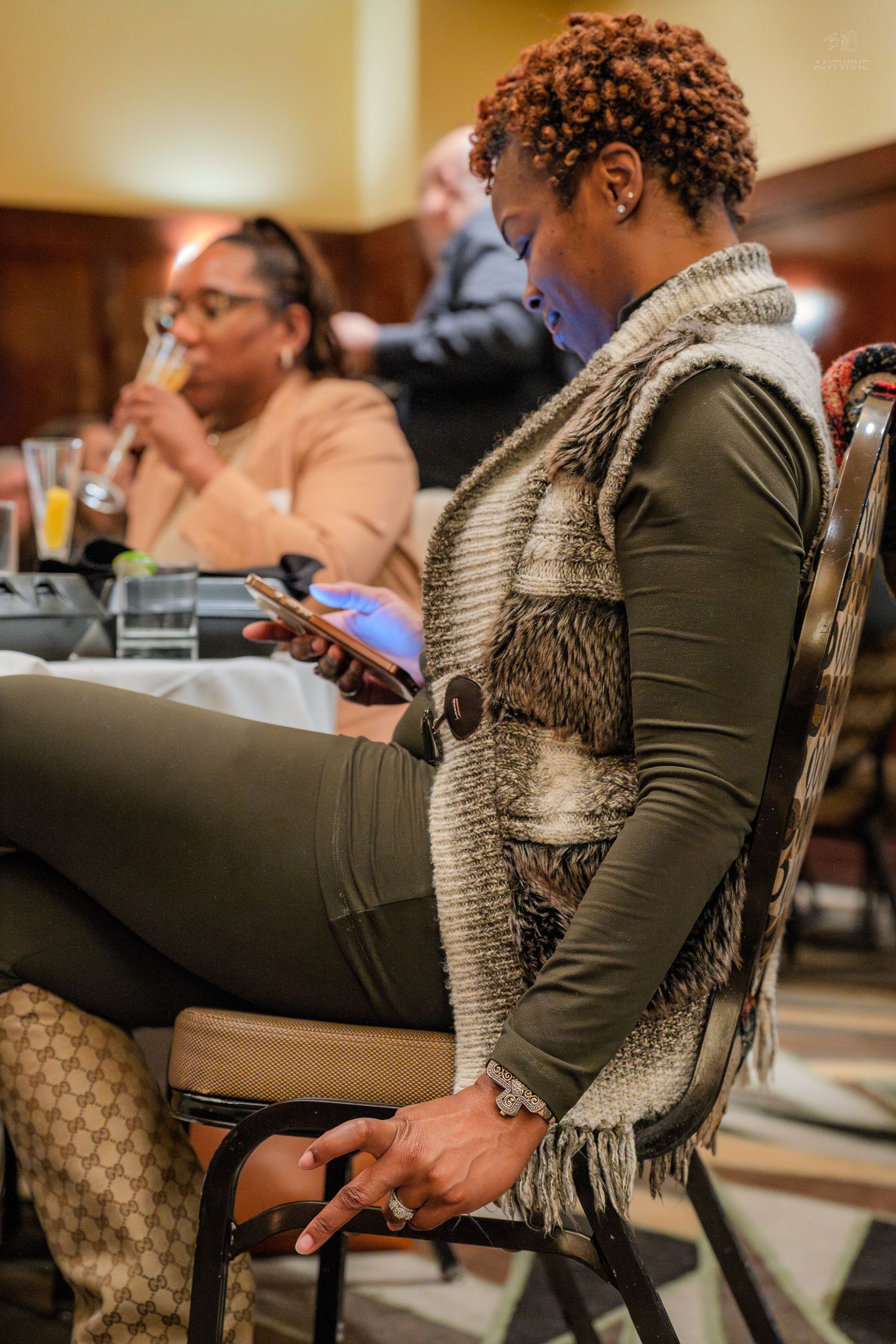 Woman in fur vest looking at tablet device while seated at indoor event.