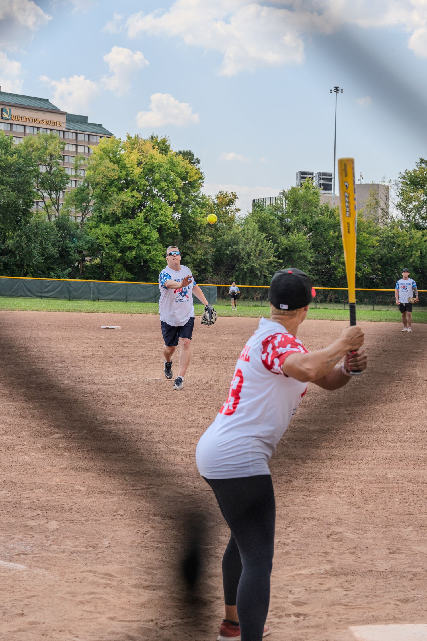 A batter swings at a yellow softball pitch during an outdoor recreational game.