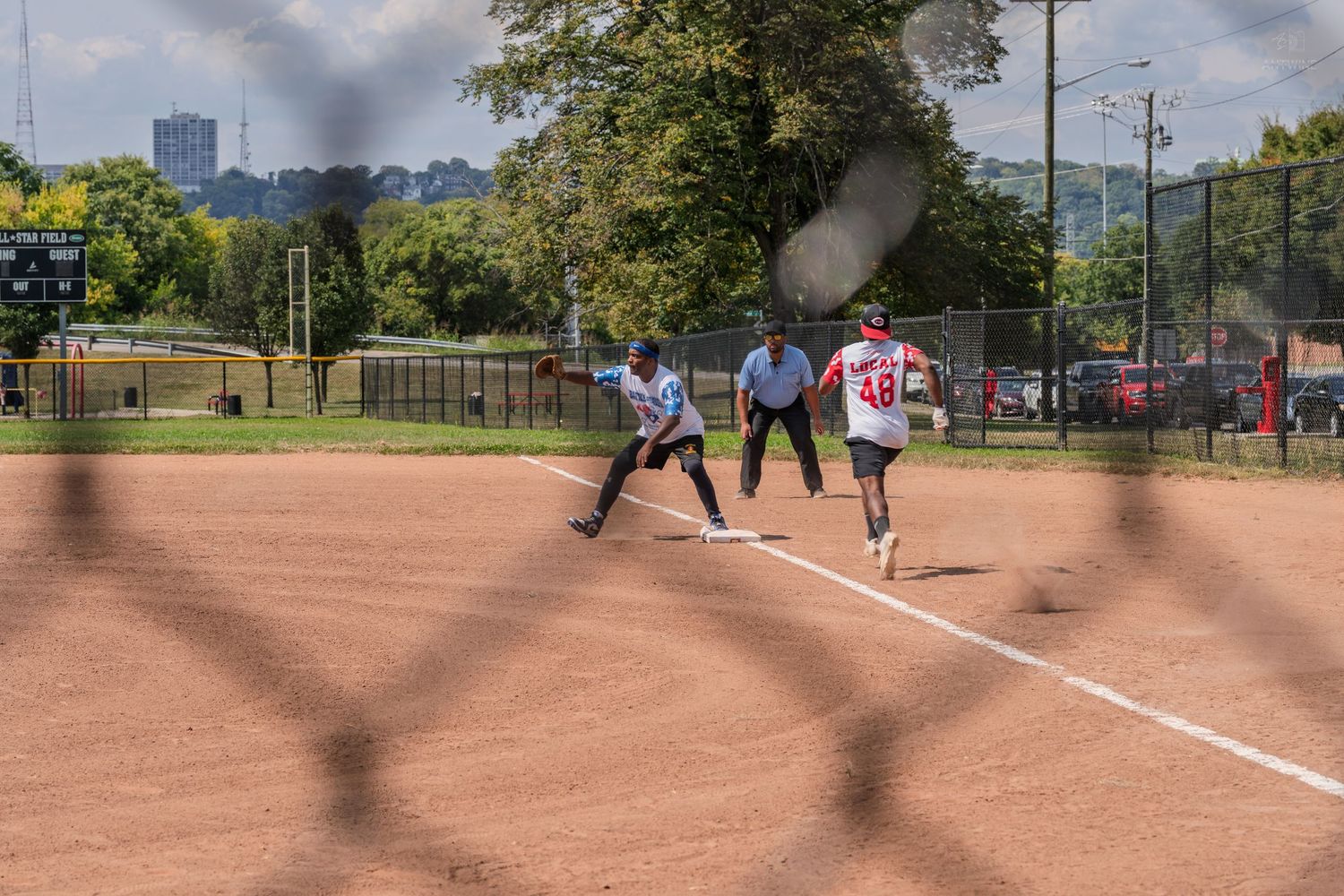 Softball player running to base as umpire signals during daytime game on dirt field.