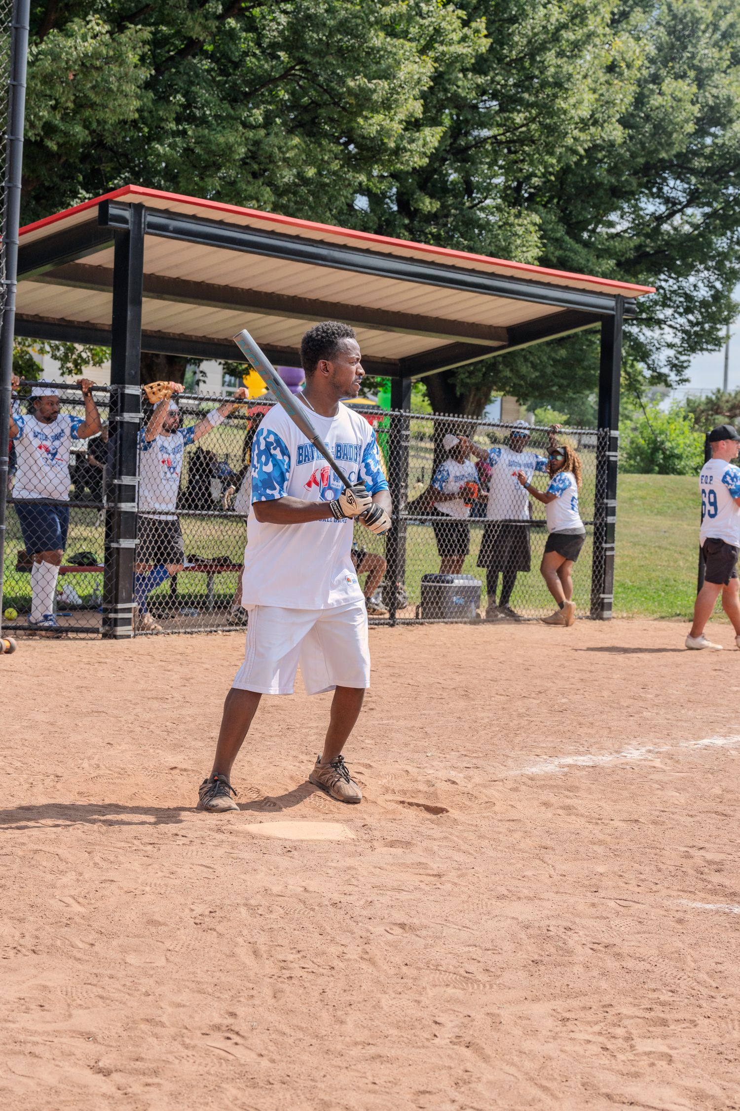 A baseball player stands at home plate holding a bat during an outdoor daytime softball game.