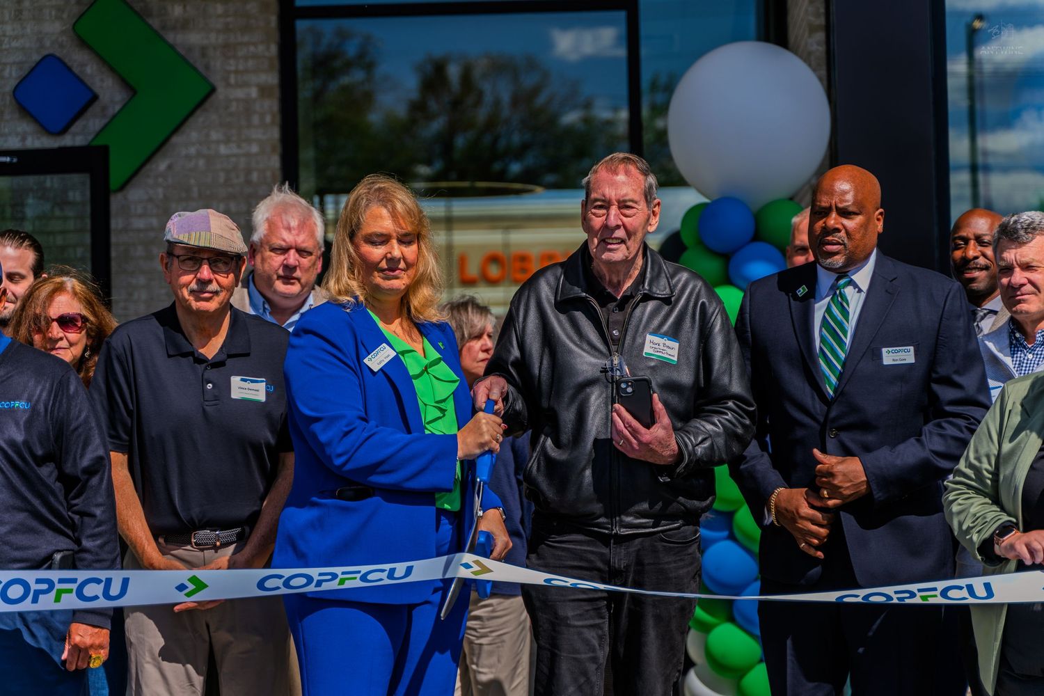 COPFCU grand opening ribbon cutting event with executives and community leaders posing outside new branch location.