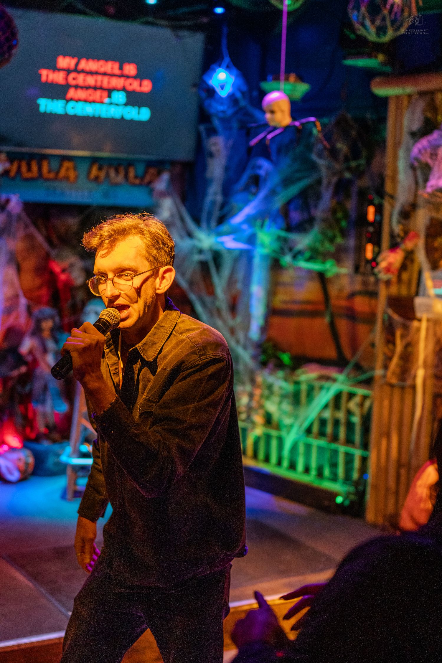 Man singing karaoke at a Halloween-themed bar with spooky decorations and colorful lights.